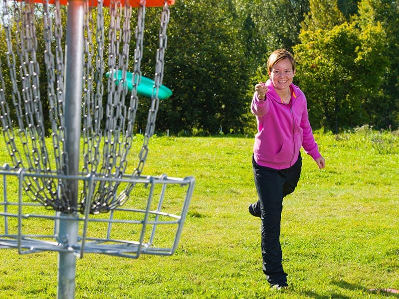 Woman throwing a frisbee into a disc golf goal.