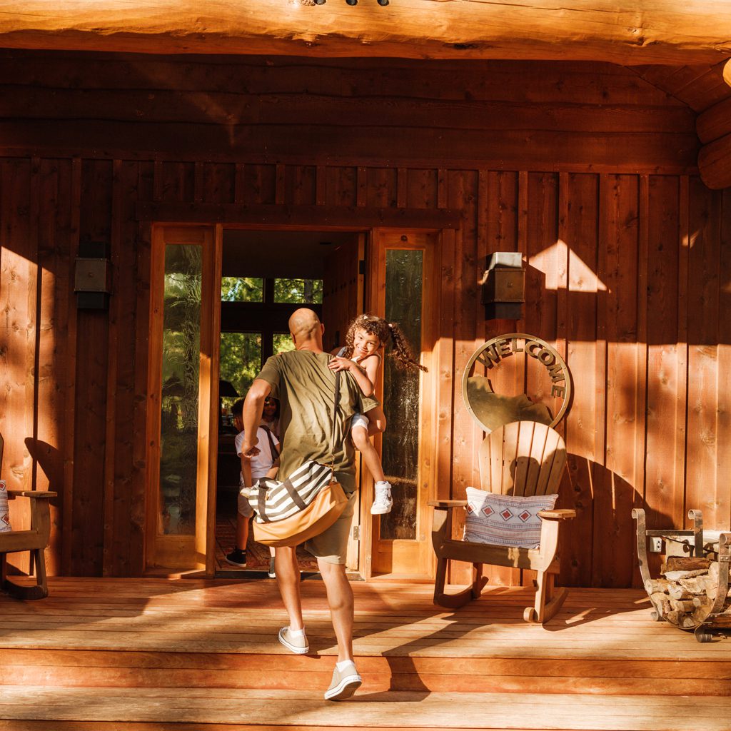 dad carrying young daughter into a cabin